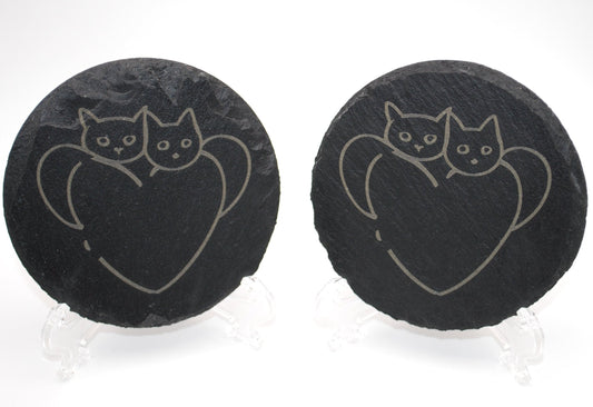 Two black slate coasters with cat and heart design on a white background