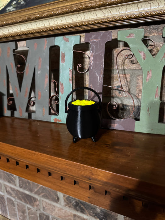 Straight-on view of the mini cauldron on a fireplace mantel, handle raised and its green potion bubbling bright