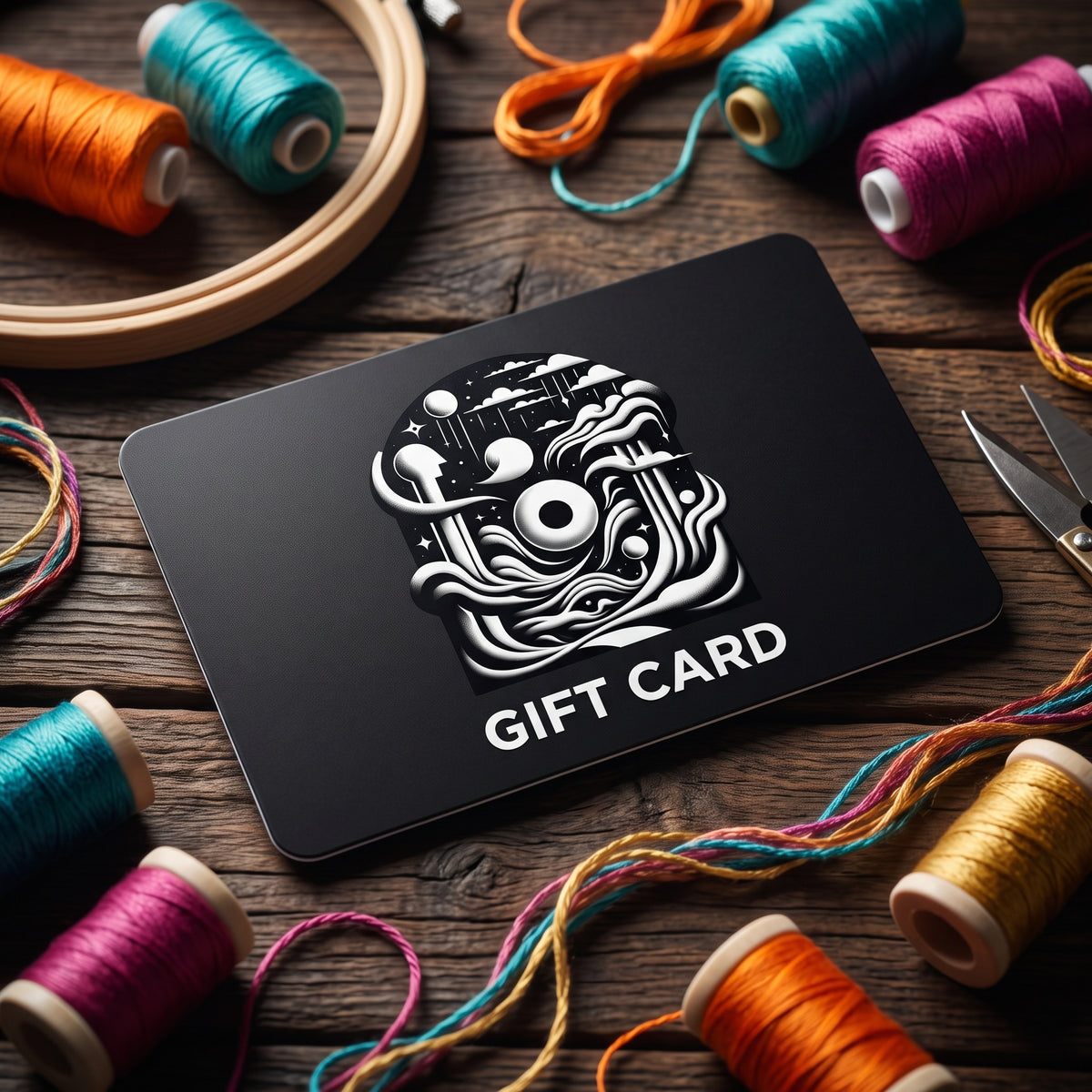 Black Its Not Nought gift card with a white logo, on a rustic wood table surrounded by colorful embroidery thread spools and a wooden hoop.