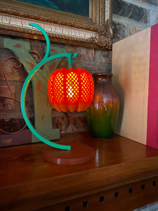 Orange 3D printed pumpkin lantern glowing on a green vine stand with a round base, lit by an LED tea light