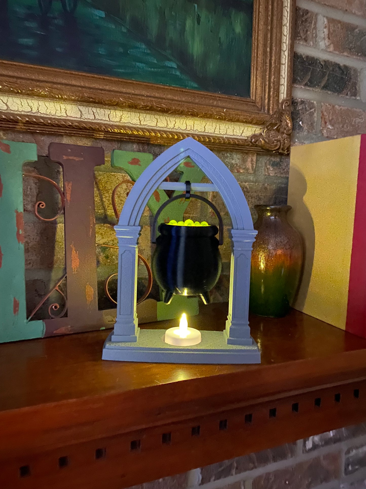 Hanging cauldron tea light holder on a wood mantel, LED tea light flickering in the stone-look base beneath the black cauldron