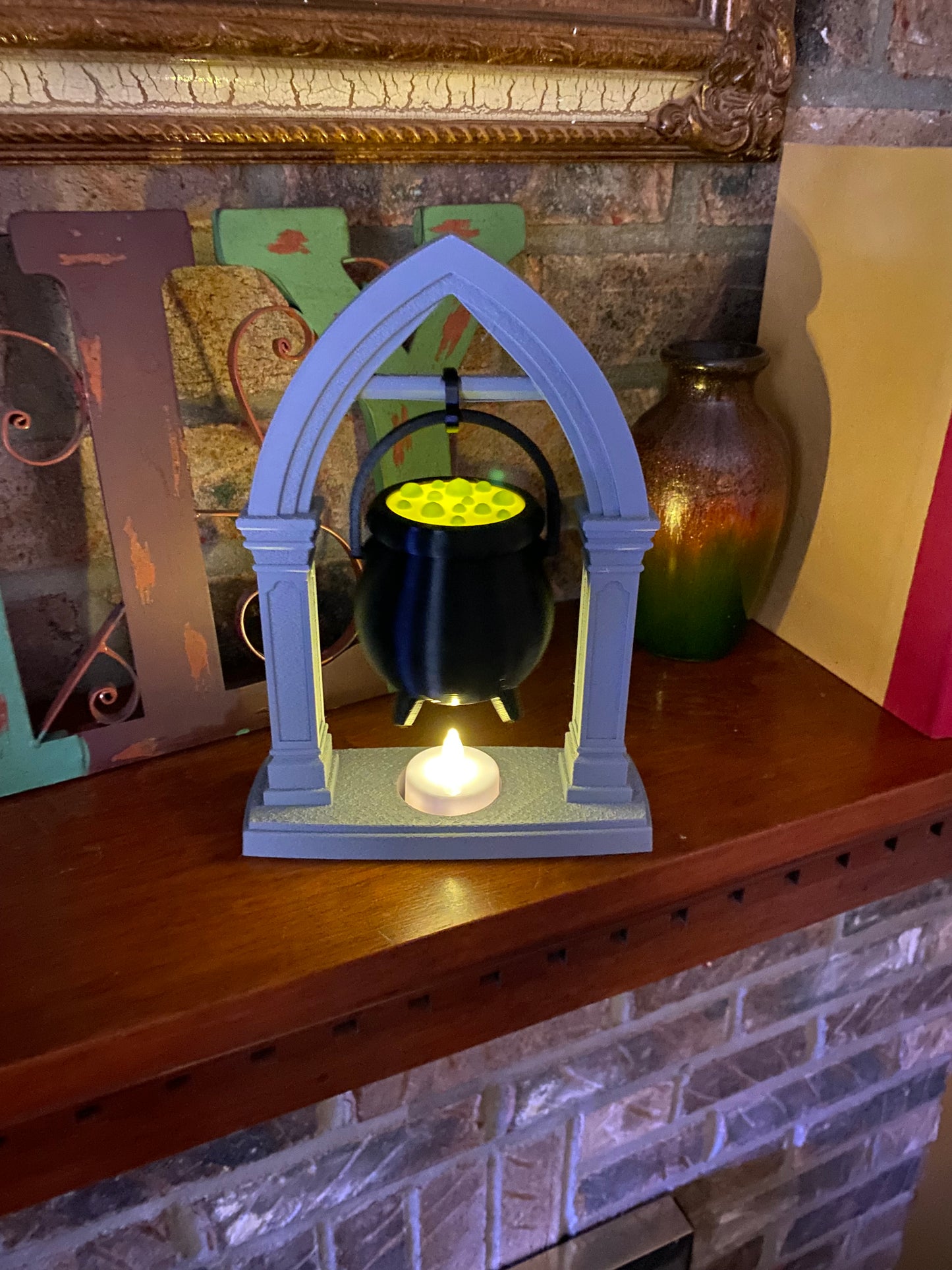 Front view of the Halloween cauldron decor piece, green potion glowing from the tea light hidden inside the hanging black pot