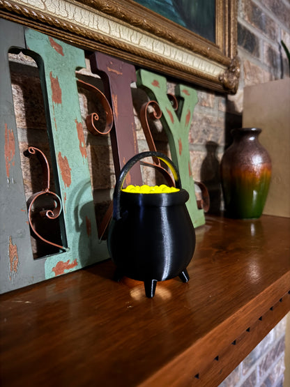 Small black cauldron standing on four feet on a mantel, its bubbling potion lit from the tea light inside