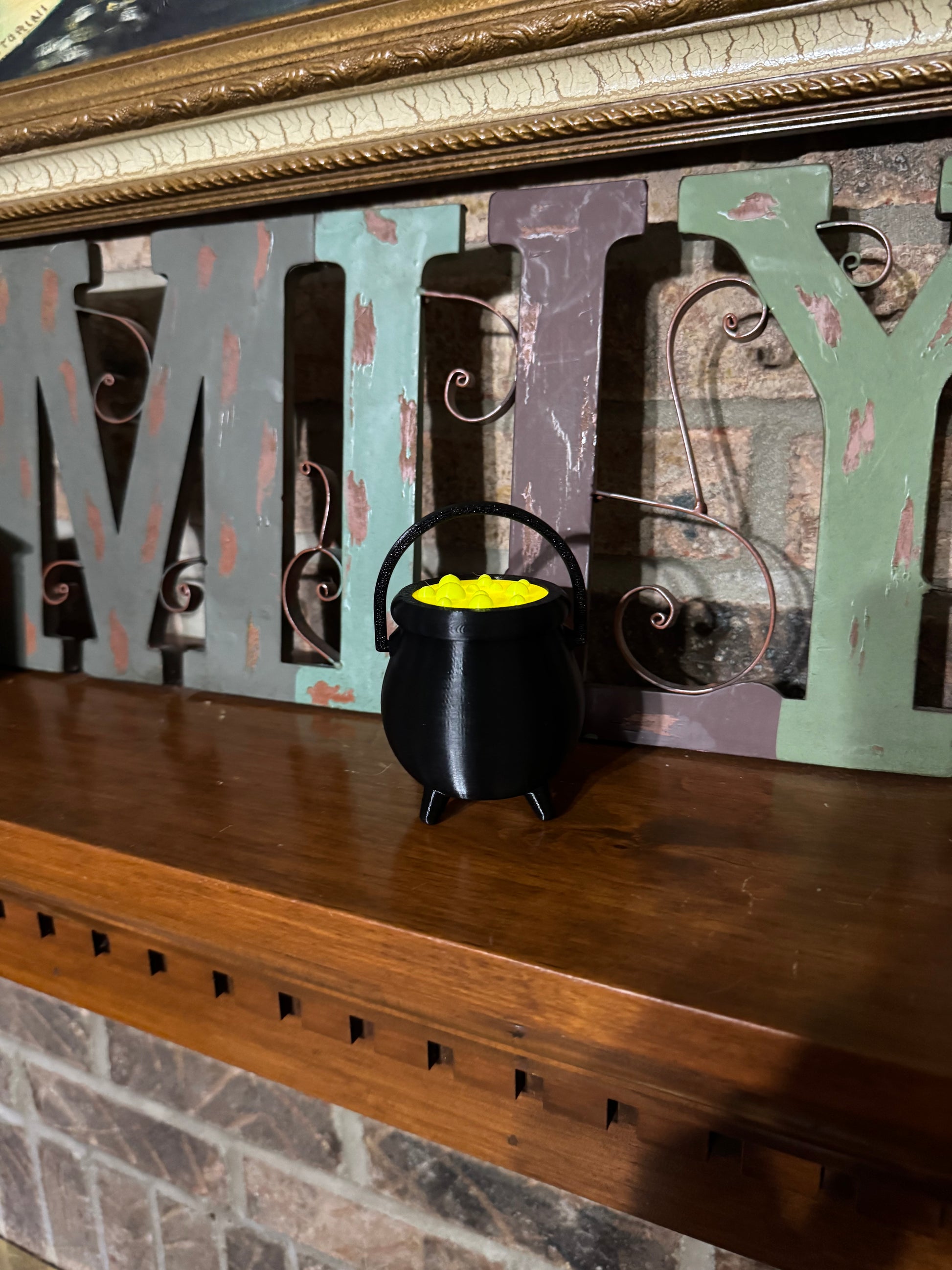Straight-on view of the mini cauldron on a fireplace mantel, handle raised and its green potion bubbling bright