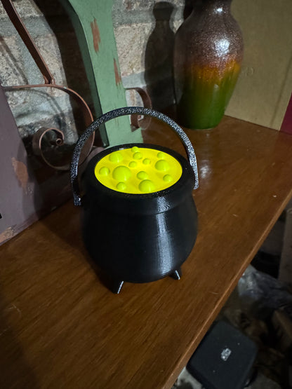 Mini black cauldron with a glowing green potion top and raised handle, 3D printed Halloween decor on a wood shelf