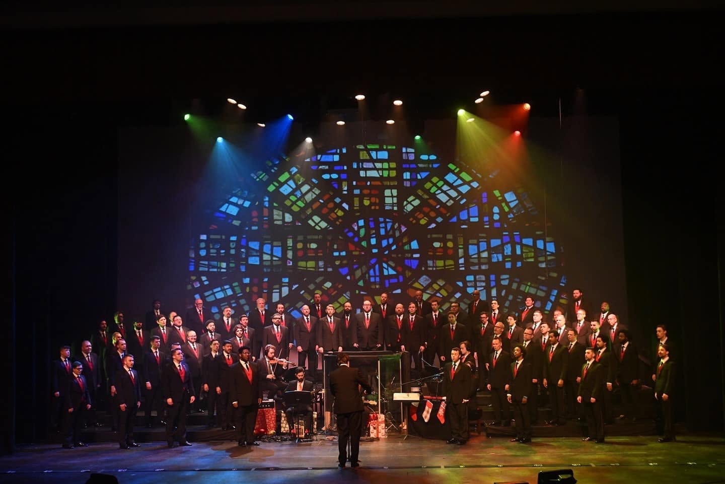 Indianapolis Men's Chorus holiday concert on risers with the number line at the stage lip, in front of a stained glass backdrop