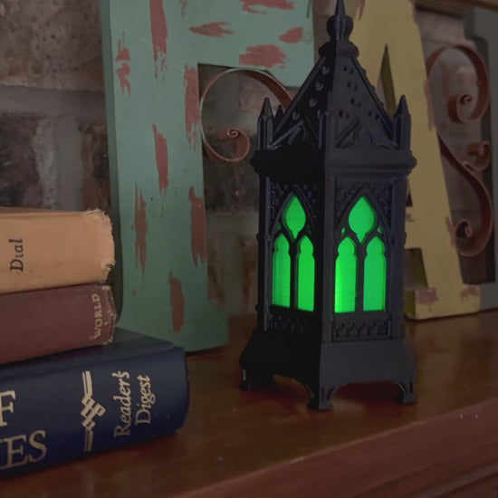 Video of a black gothic cathedral lantern with green glowing windows, moving in close on the pointed-arch tracery and back out.